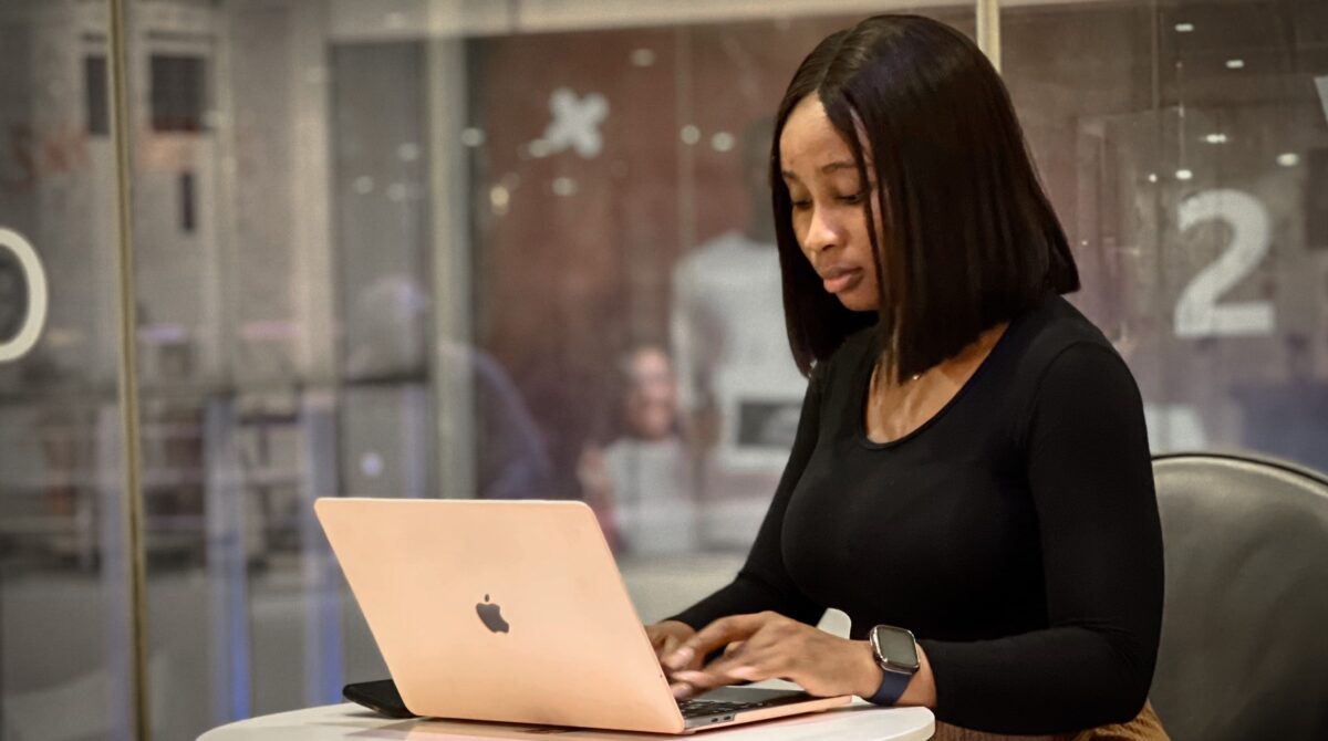 A young woman with brown skin and brown hair sits at a laptop.